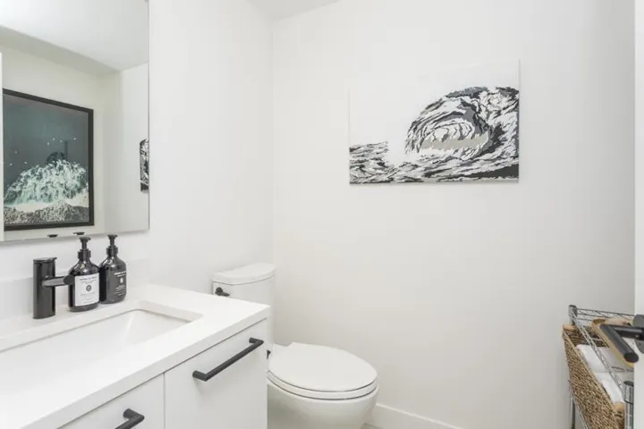 White vanity with integrated sink, sleek black faucet, and frameless mirror