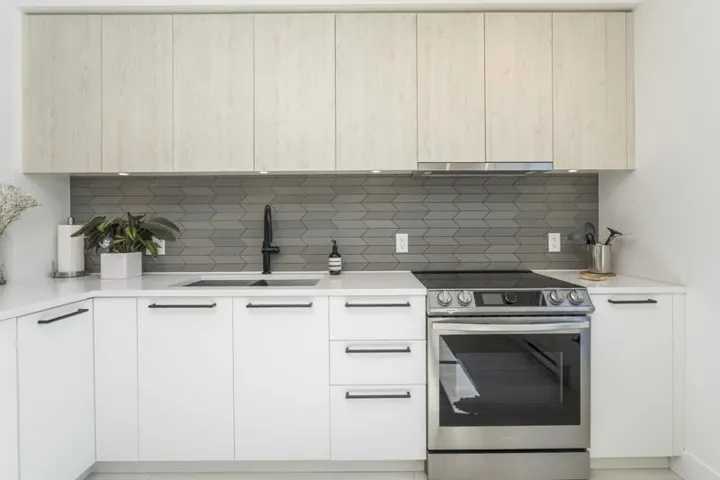 White cabinetry, wood-finish upper cabinets, stainless steel range, white countertops, and a gray chevron tile backsplash