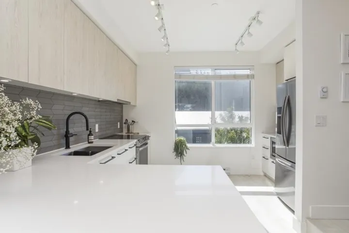 Modern kitchen featuring light wood-finish cabinetry, a white countertop, a dark chevron-patterned tile backsplash, a matte black faucet, and stainless steel appliances