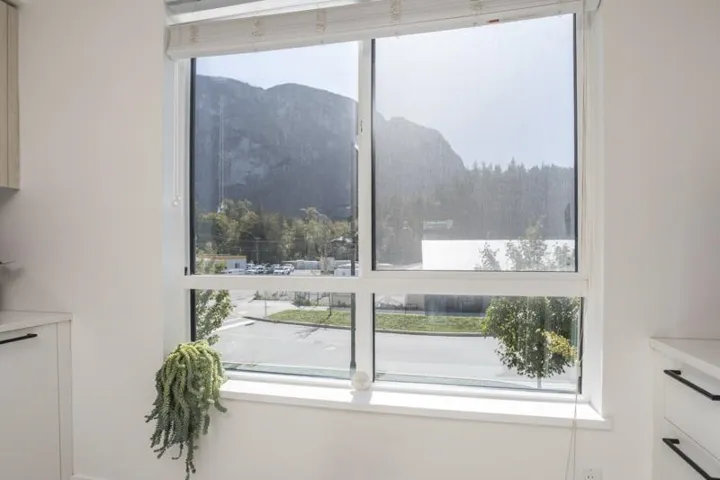 White framed window with integrated blinds, offering a streetscape and mountain backdrop