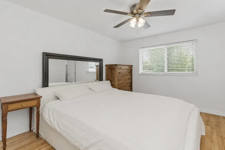 Bedroom featuring light wood-finish flooring, a window with blinds, and a ceiling fan with integrated lighting