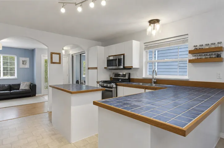 White cabinetry with stainless steel appliances, blue tiled countertops, and wood-finish trim
