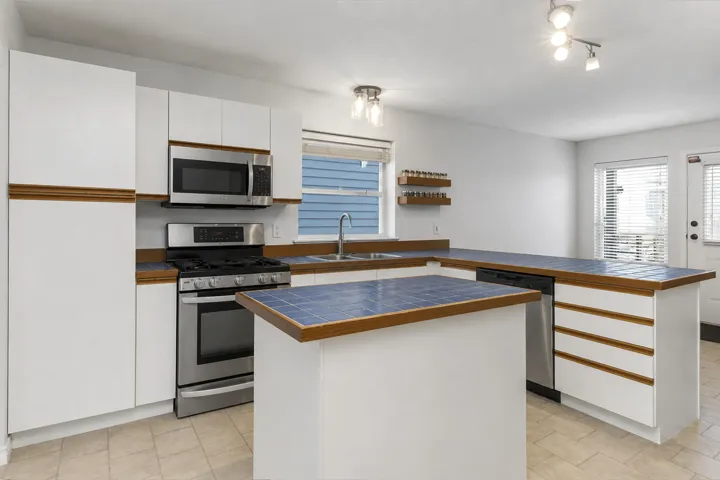 Kitchen featuring white cabinetry with wood-finish accents, blue tile countertops, and stainless steel appliances