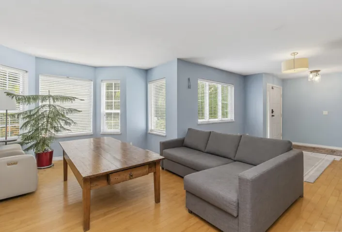 Living space featuring light wood-finish flooring, multiple windows with blinds, and light blue wall paint