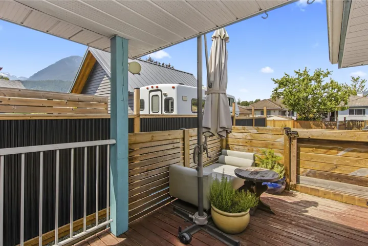 Covered outdoor deck area featuring wood-finish flooring, slatted wood fencing, and a white railing