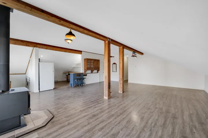 Living room with a wood stove, lofted ceiling with beams, wood finished floors, and a baseboard heating unit