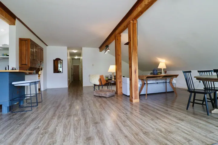 Open-concept living space featuring wood-finish flooring, exposed timber beams, a breakfast bar, and a sloped ceiling