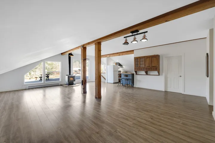 Unfurnished living room featuring a wood stove, vaulted ceiling with beams, wood finished floors, and a baseboard heating unit