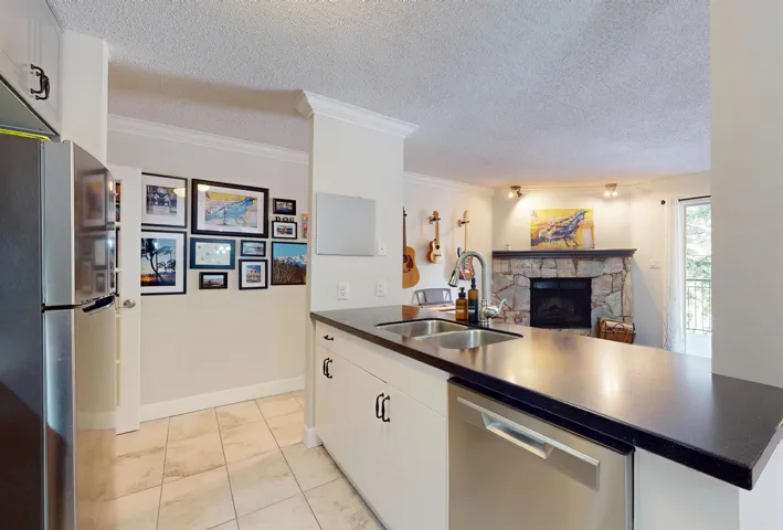 Kitchen featuring appliances with stainless steel finishes, a sink, dark countertops, a fireplace, and open floor plan