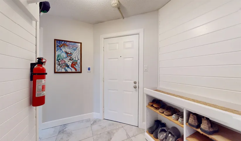 Mudroom with light marble finish flooring, wooden walls, a textured ceiling, and baseboards