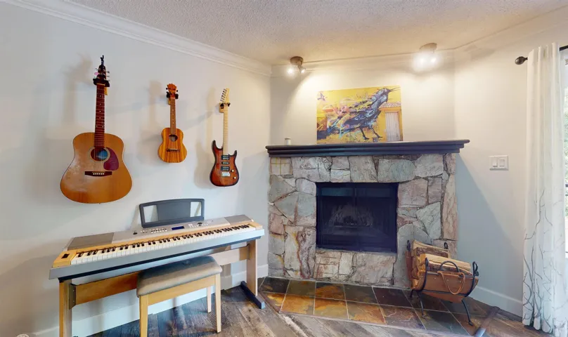 Living area featuring a textured ceiling, ornamental molding, baseboards, wood finished floors, and a stone fireplace