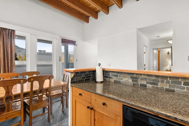 Kitchen with freestanding refrigerator, dark colored carpet, track lighting, a wooden ceiling with exposed beams, and a center island