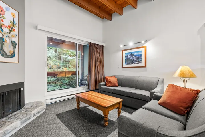Carpeted living area featuring a fireplace with raised hearth, a wooden ceiling with exposed beams, and a baseboard heating unit