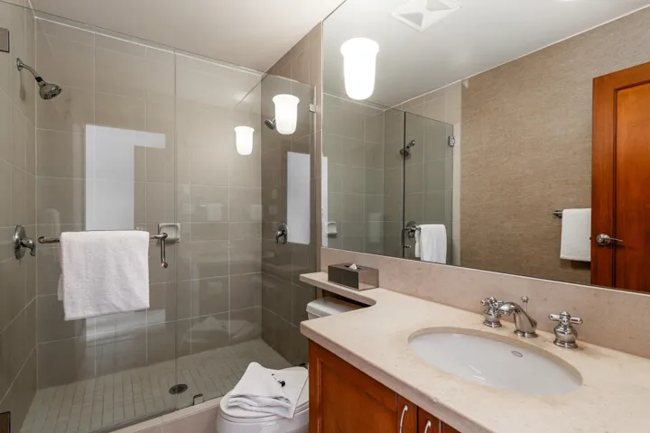 Contemporary bathroom featuring a spacious glass-enclosed shower with tile surround, an extended vanity with an integrated sink, a large wall-mounted mirror, and wood cabinetry