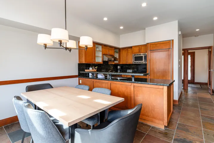 Open-concept dining area and kitchen featuring warm wood-finish cabinetry, dark stone countertops, and a full suite of stainless steel appliances