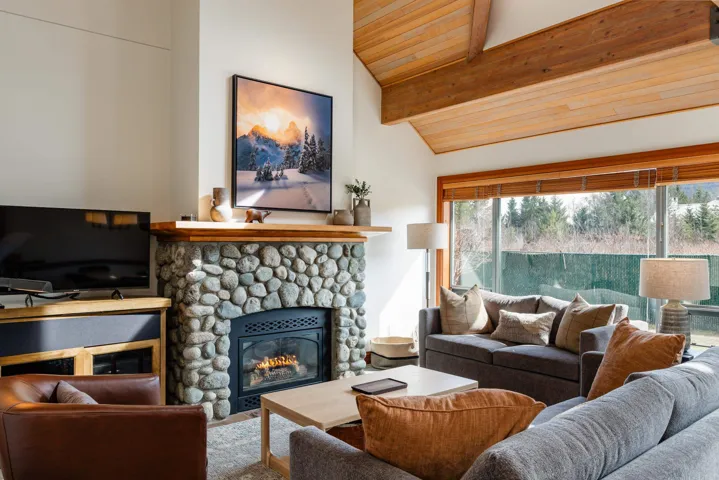 Living area featuring a stone fireplace with a wood mantle, vaulted wood-paneled ceilings with exposed beams, and large picture windows