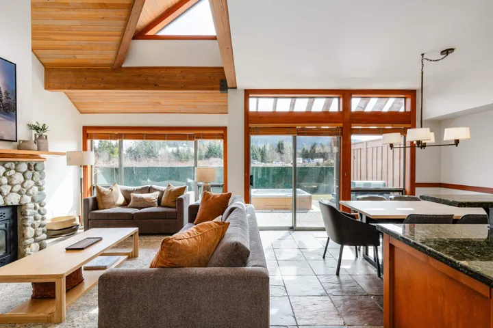 Spacious living area featuring a vaulted wood-finish ceiling with exposed beams, a stone-surround fireplace, and large sliding glass doors opening to the exterior deck
