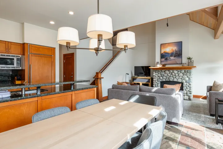 Open-concept living space featuring a stone fireplace, wood-finish flooring, and a kitchen island with a dark countertop