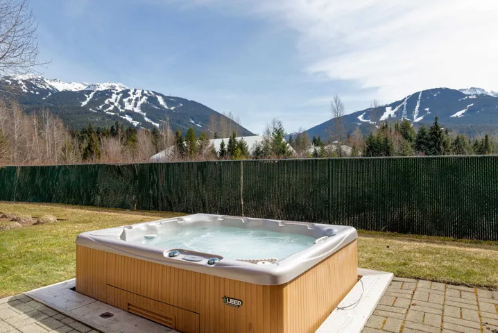Outdoor spa tub set on paver patio, surrounded by a grassy area and privacy fencing