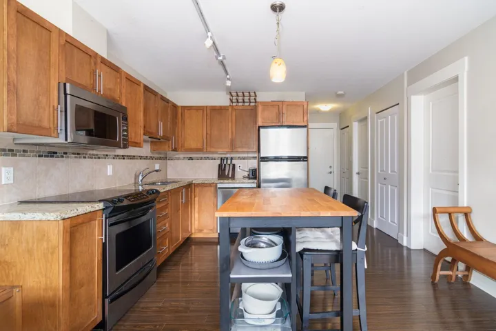Kitchen featuring hanging light fixtures, dark wood-style flooring, stainless steel appliances, and decorative backsplash