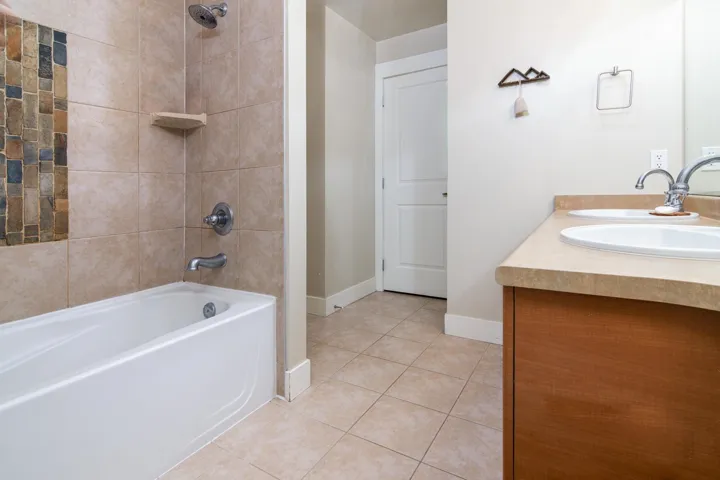 Full bath featuring double vanity, shower / bathtub combination, a sink, baseboards, and tile patterned floors
