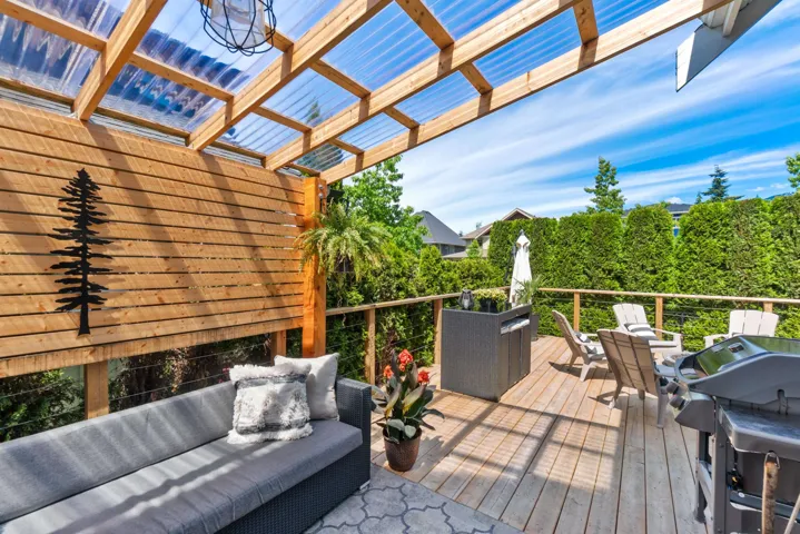 Expansive wood-finish deck featuring a clear panel pergola, slatted wood privacy wall, and cable railing system