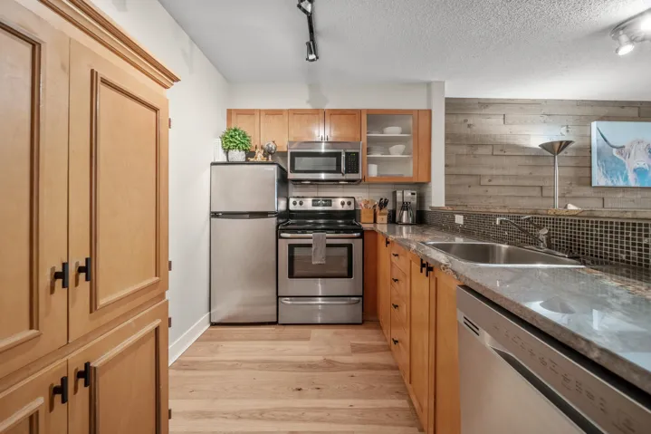 Kitchen featuring stainless steel appliances, a sink, decorative backsplash, light wood-type flooring, and glass insert cabinets