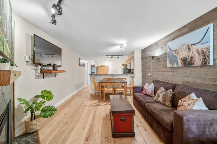 Living room with track lighting, wooden walls, light wood-type flooring, an accent wall, and a textured ceiling