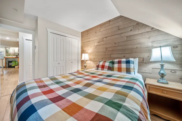 Bedroom featuring vaulted ceiling, wooden walls, wood finished floors, and a closet