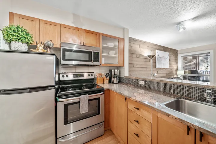 Kitchen with appliances with stainless steel finishes, decorative backsplash, a sink, glass insert cabinets, and a textured ceiling