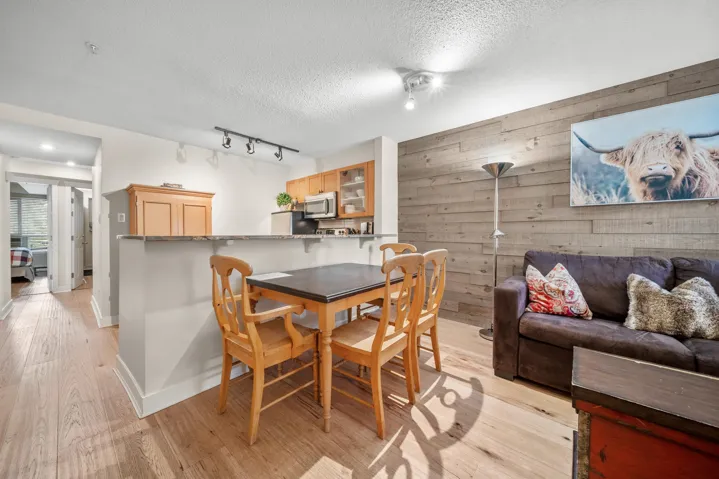 Dining room with wooden walls, a textured ceiling, light wood-style floors, rail lighting, and baseboards