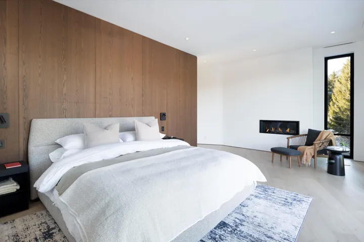Bedroom featuring a glass covered fireplace, wood walls, light wood-style flooring, and recessed lighting