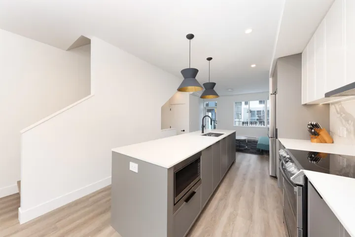 Kitchen with light countertops, a sink, light wood finished floors, appliances with stainless steel finishes, and a center island with sink