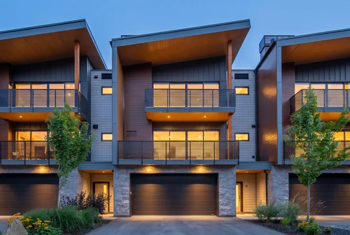 Contemporary townhome featuring multiple balconies with glass railings, two integrated garages with roll-up doors, and stone facade accents