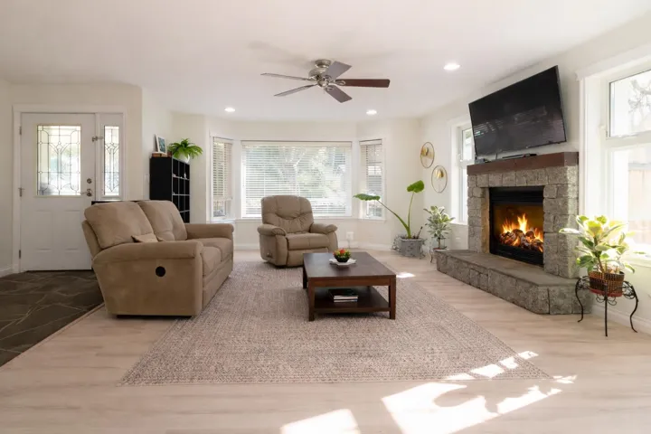 Living area featuring wood finished floors, a stone fireplace, plenty of natural light, a ceiling fan, and recessed lighting