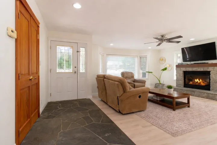 Living room with a stone fireplace, wood finished floors, a ceiling fan, and recessed lighting