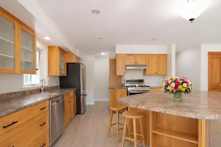 Kitchen featuring stainless steel appliances, glass insert cabinets, light wood-style flooring, a kitchen breakfast bar, and recessed lighting