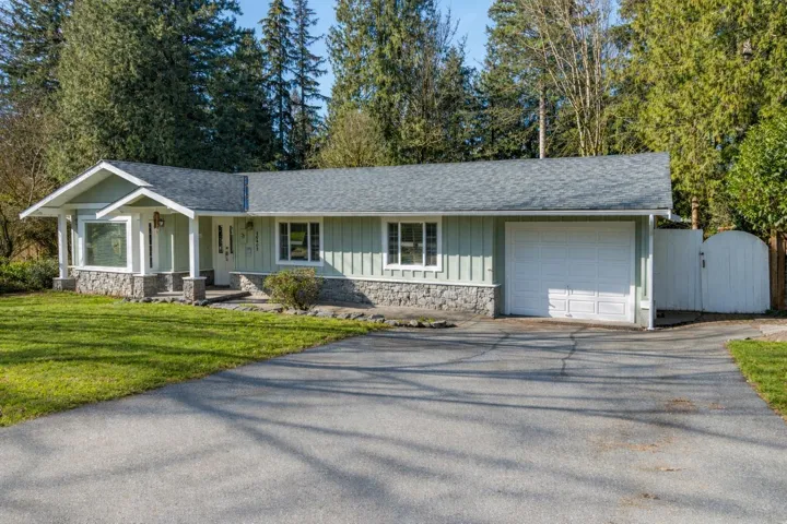Ranch-style home featuring stone siding, driveway, an attached garage, and a shingled roof