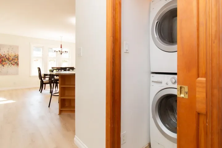 Laundry area featuring light wood-type flooring, stacked washer and dryer, and a chandelier