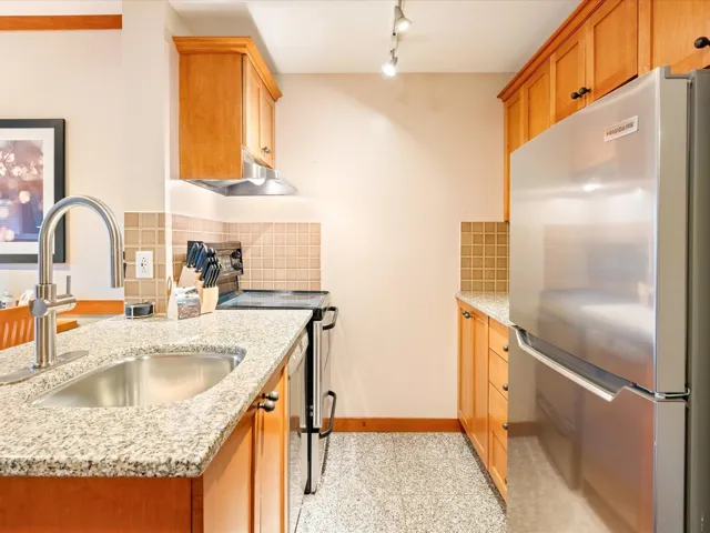 Kitchen with appliances with stainless steel finishes, decorative backsplash, light stone countertops, brown cabinets, and under cabinet range hood