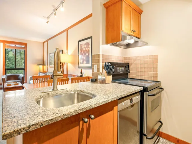 Kitchen featuring appliances with stainless steel finishes, under cabinet range hood, light stone countertops, tasteful backsplash, and rail lighting