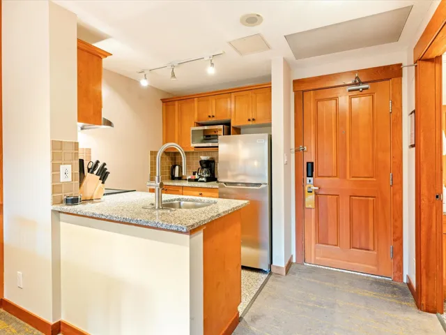Kitchen with stainless steel appliances, a peninsula, backsplash, and light stone countertops