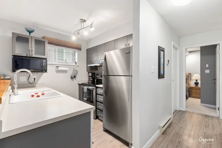 Kitchen featuring stainless steel appliances, wood-finish flooring, track lighting, a window with blinds, and white countertops