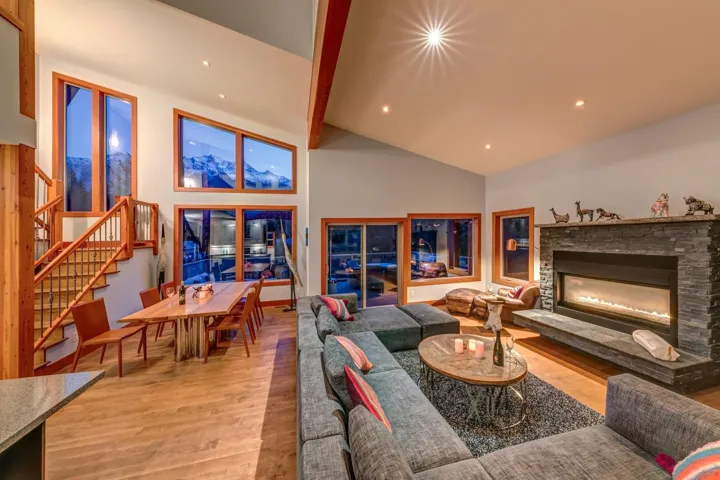 Living room featuring a fireplace, wood finished floors, beam ceiling, stairs, and high vaulted ceiling