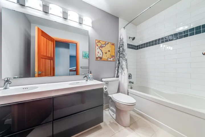 Full bath with shower / bath combo, double vanity, toilet, and tile patterned flooring