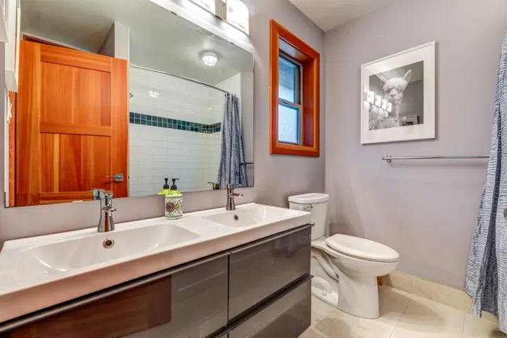 Bathroom featuring toilet, double vanity, a shower with curtain, and tile patterned floors
