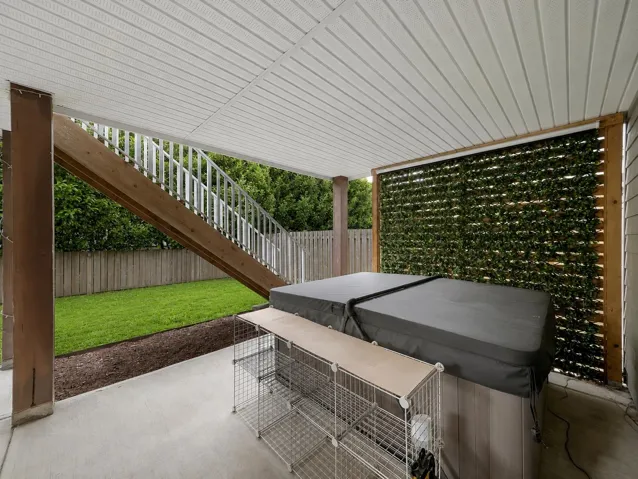 Covered patio area featuring a hot tub, concrete flooring, and a decorative green screen wall