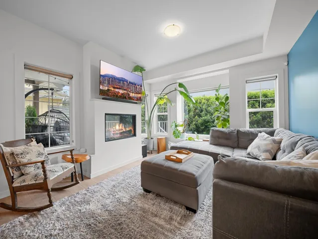 Living room featuring a built-in linear fireplace, large windows, wood-finish flooring, a tray ceiling, and a prominent accent wall