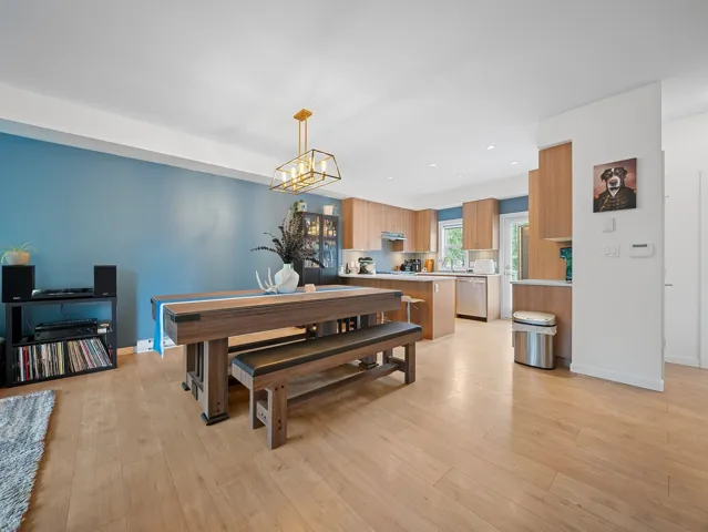 Open-concept living space featuring wood-finish flooring, a modern chandelier, and light wood-finish cabinetry in the kitchen
