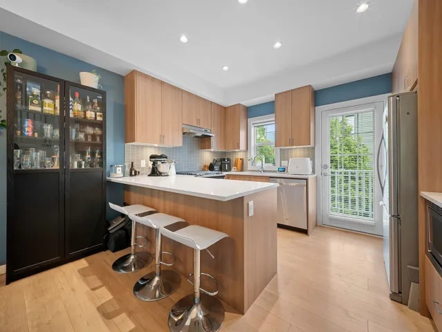 Modern kitchen featuring light wood-finish cabinetry, white countertops, and a white tile backsplash